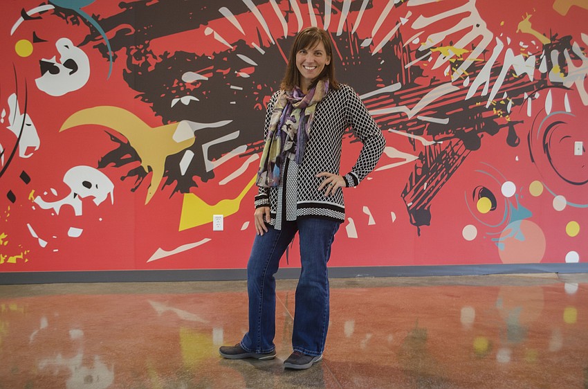 Ringling alum Julie Kanapaux stands in front of the mural she created for the new library.  The mural represents the impact of technology on the creative process. 
