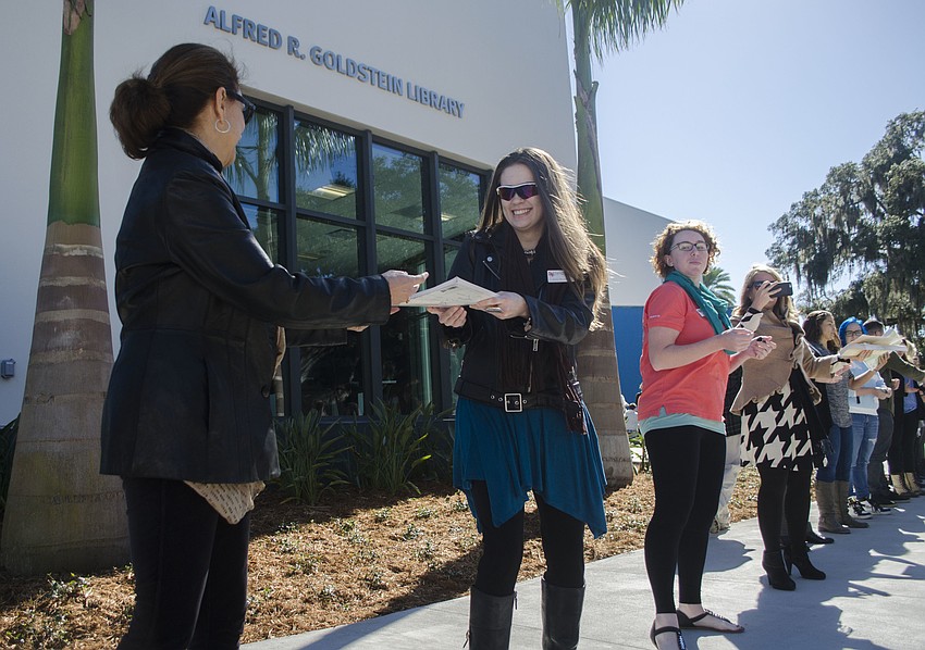 Nancy Long and Arianna Westerfield pass books in front of the new Alfred R. Goldstein Library.