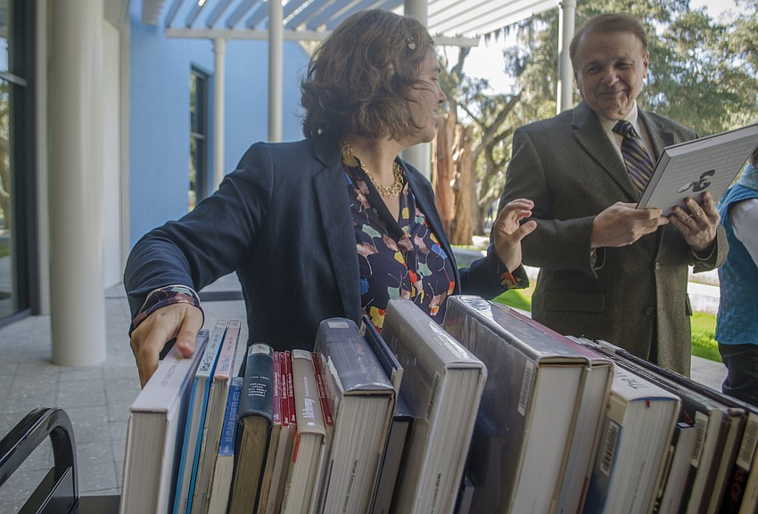 Director of Library Services Kristina Keough places books on shelves as Ringling College of Art and Design President Larry Thompson passes her a book.