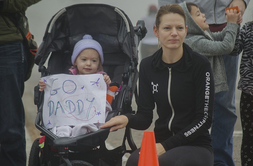 Pennie Riches sits next to Poppy Riches while she holds a sign and waits for her father to make the final turn.