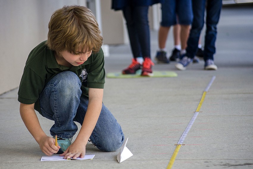Xander Levine measures how far he threw his paper airplane.
