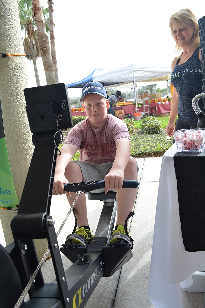 Dylan Kasper, 15, tests his rowing stamina at Powerhouse Row and Fitness'   s booth. Co-owner Bev Kinder shows him what to do.