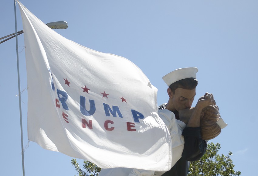 A Trump campaign flag waves in the wind in front of the Unconditional Surrender statue.