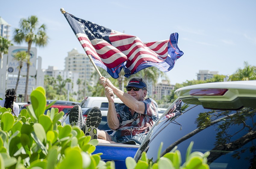 Larry Tatsch waves a flag from the bed of a truck parked in the Bayfront Park parking lot.
