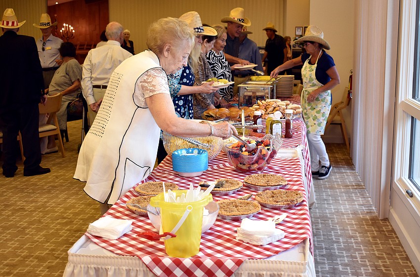 Attendees piles their plates with items from the buffet including hot dogs, fruit salad and pie.