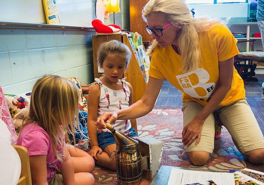 Beekeeper Agnes Kubolicz shows Skylar Chapnick-Rodriguez and Claire Bragg how a bee smoker works.