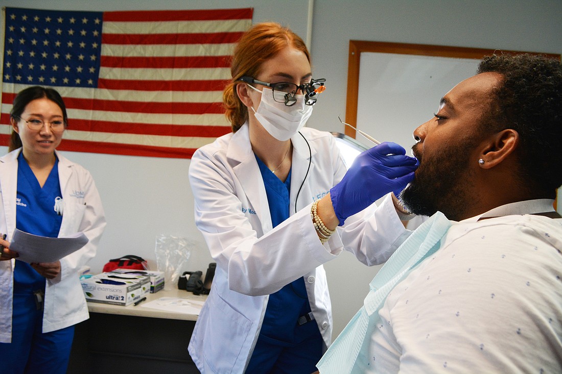 LECOM dental student Mary Moore completes a dental exam on U.S. Coast Guard veteran Eric Davis as fellow student Phennatda Polpornvitoon, behind, documents findings.