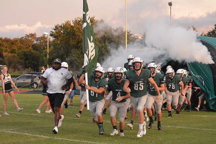 The Mustangs take the field through a stream of smoke.