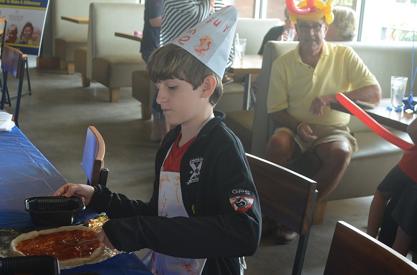 Safety Harbor's Ryan Stewart, 13, wears his apron and hat that he made at the event while he makes his pizza.