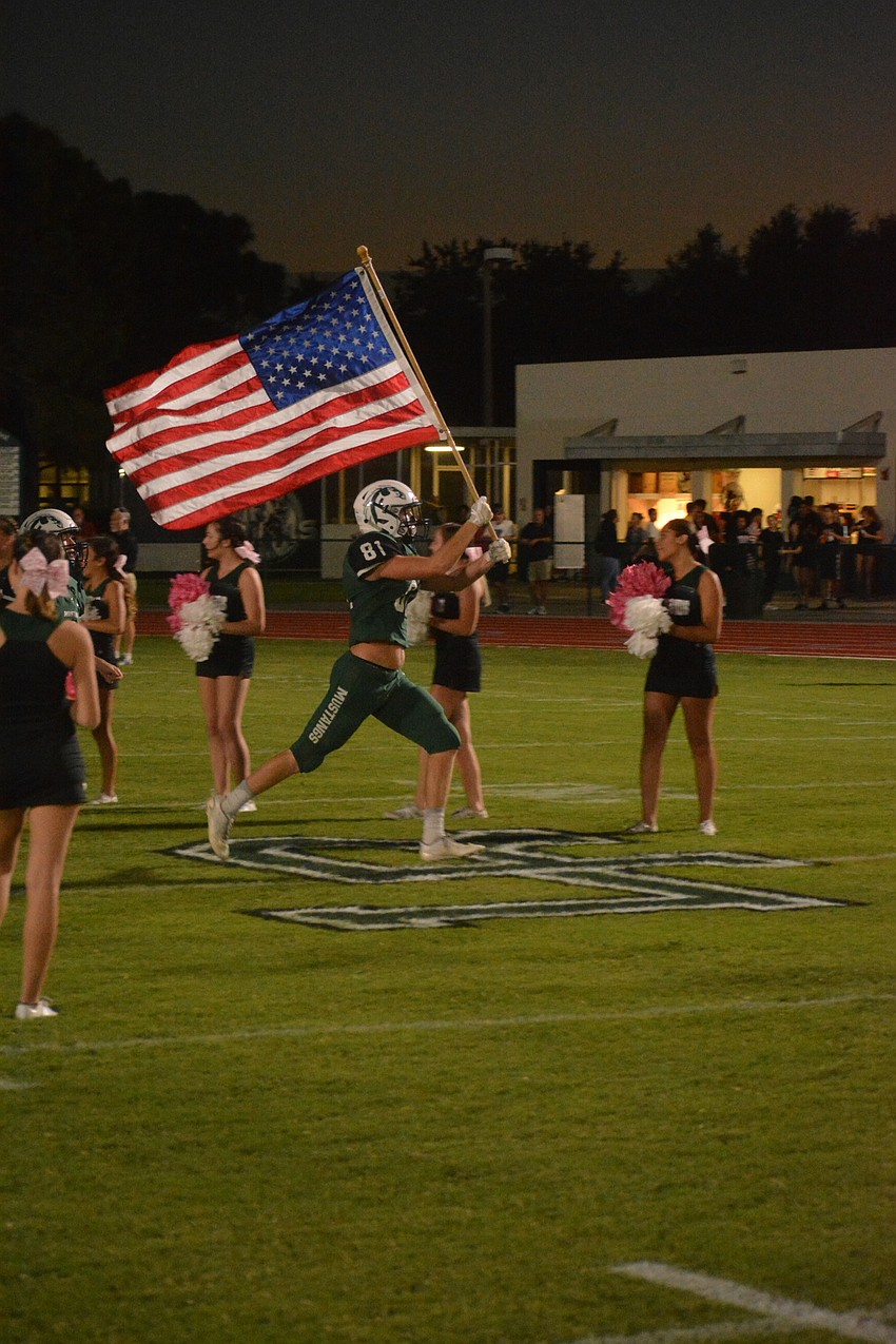 Mustangs senior wideout Cooper Corley leads the team onto the field, American flag in hand.