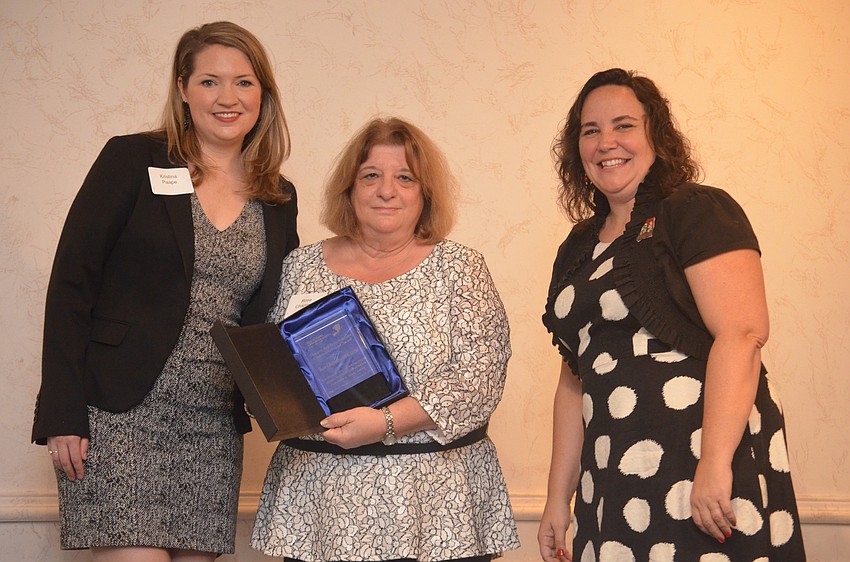 Kristina Paape (left) and Arin Morris (right), present the Howard and Betty Isermann Community Impact Award to Rose Chapman (center).