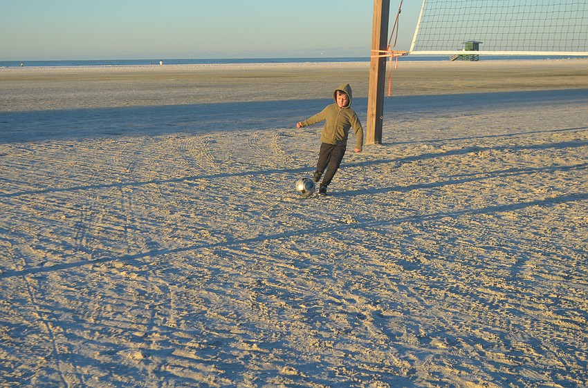 Liam Murray plays soccer on the beach as the sun rises.