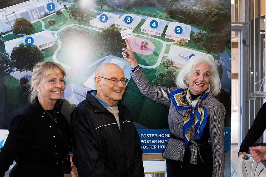 Dorothea Sandland, Ernie Kretzmer and Graci McGillicuddy pose next to the photo of the residential home Kretzmer funded.