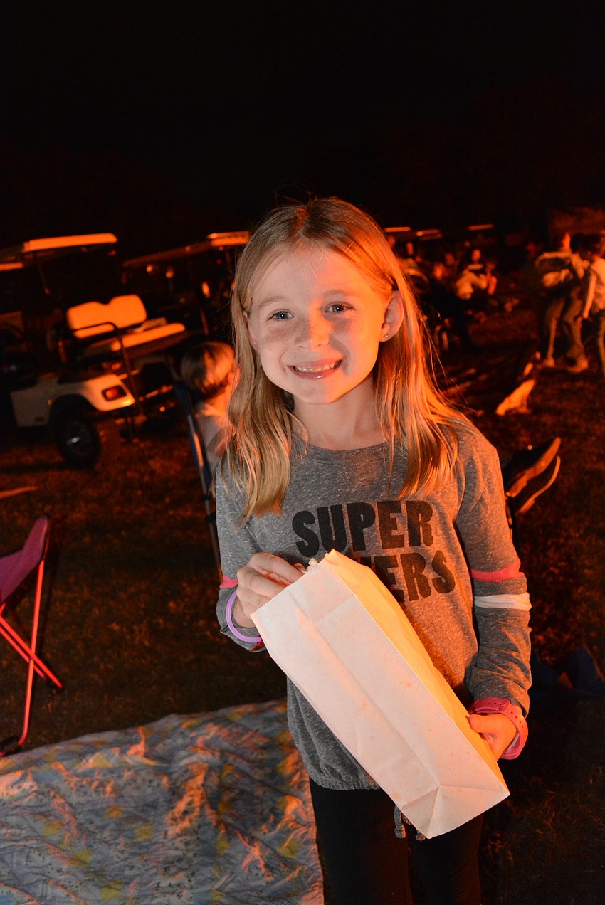 First-grader Cooper Eidson munches on popcorn as she finds friends and family around the bonfire.