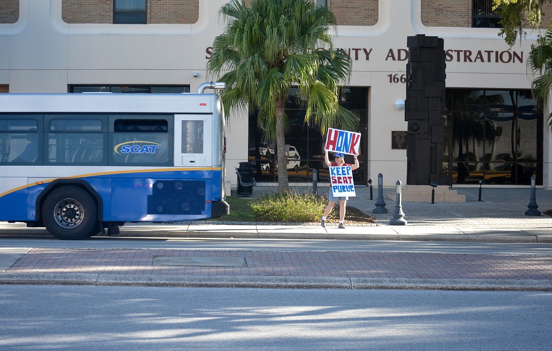 Chris Tapalaga watches as a SCAT bus drives by her as she protests in front of the County Administration building.
