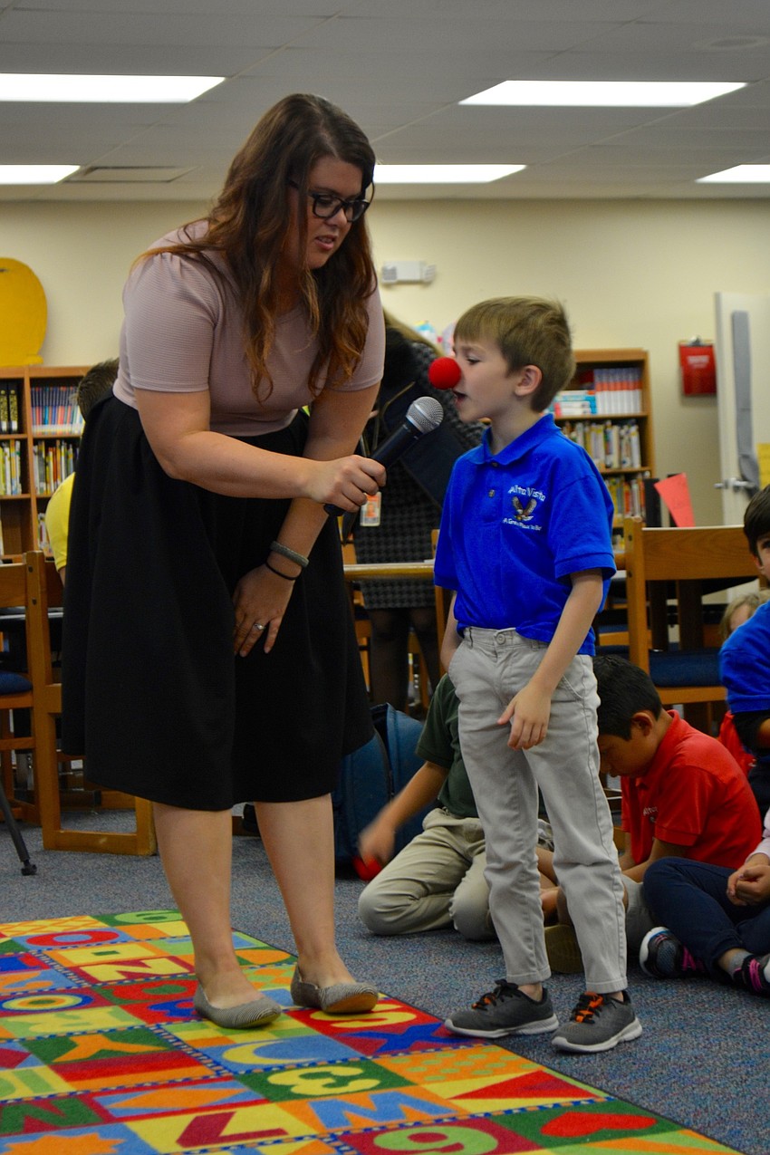 Second-grade teacher Faith Piper holds a microphone as a second-grade student named Keanu explained that Independence Day in the United States is celebrated on July 4.