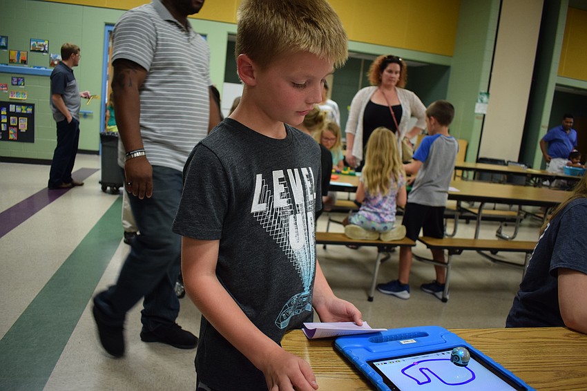 Second-grader Connor Keenan watches a tiny robot follow a path drawn on a tablet.