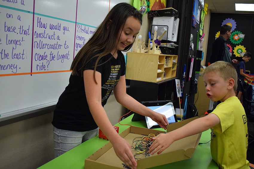 Elizabeth Sponsel, a fifth grader, explains the mechanics and process by which students were able to make a larger-than-life floor piano that makes sounds when the keys are stepped on, while first grader Zachary Malson watches.