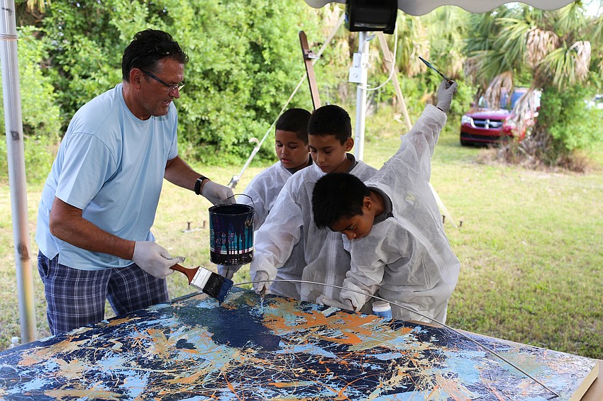 Miro Czekanski shows Daniel Delcid, Emiliano Torres and Breyon Peterson how to paint on the canvas.