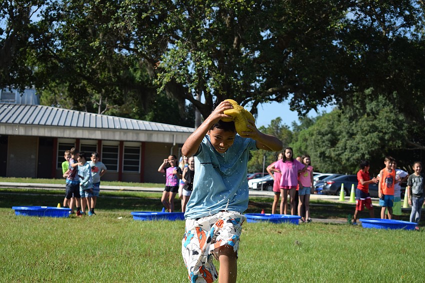 Fabrizio Sanchez, a fourth grader in Brijete France's class, competes in a relay race where he has to hold a sponge on top of his head, squeeze  it out in a bucket and run back.