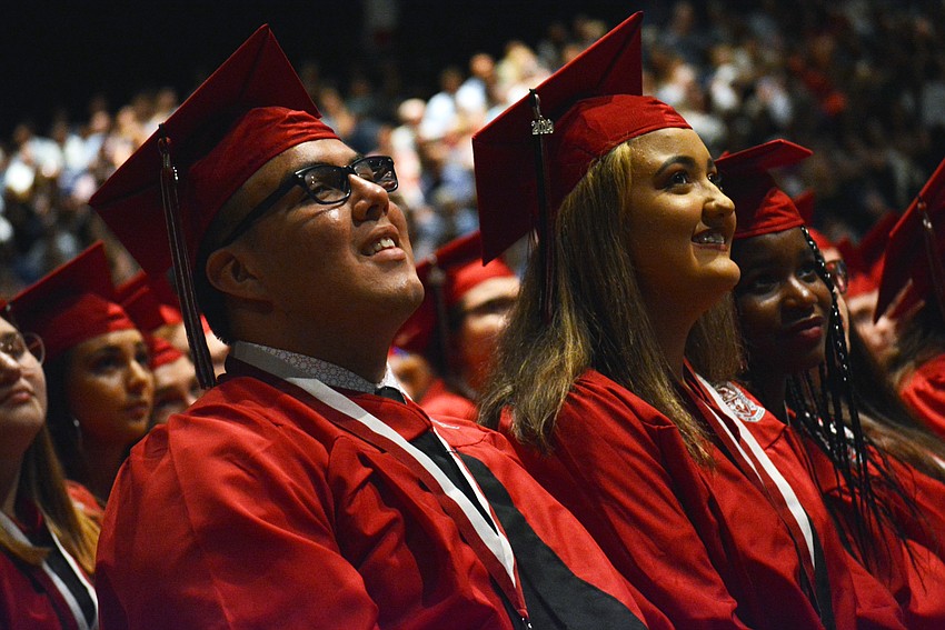 Juan Aguilar Perez grins as he sees photos of friends flash on a screen. A slideshow of senior pictures is shown after graduates are seated.