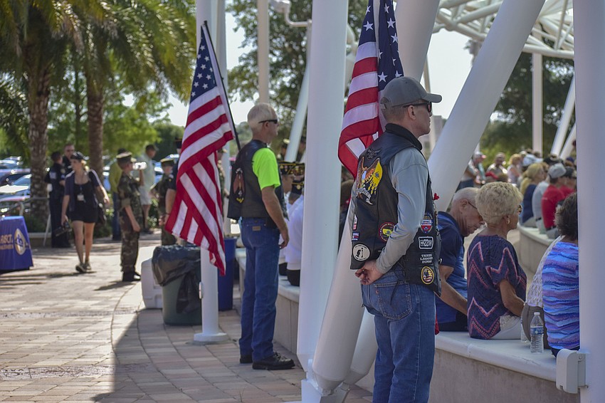 Veterans stand with Amerian flags behind the crowd of people.