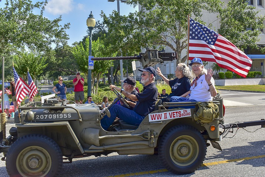 World War II veterans smile and wave to the crowd while riding down Main Street.