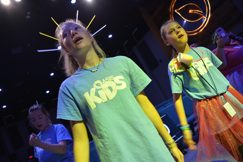 Teenage volunteers Savannah Langei and Kaylin Kitchens lead preschoolers in movements for a song they are performing on stage.