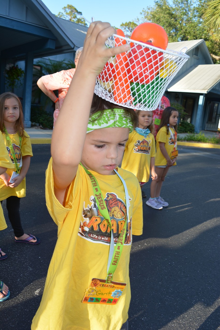 Six-year-old Grant Pecora tries to balance a bucket of fruit on his head.