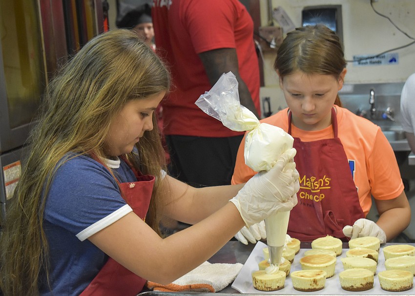 Sofia Della Vedova and Sarah Gray take turns pipping whipped cream on cheesecake.