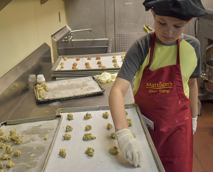 Liam Dalton prepares cookie sheets with chocolate chip cookie dough.