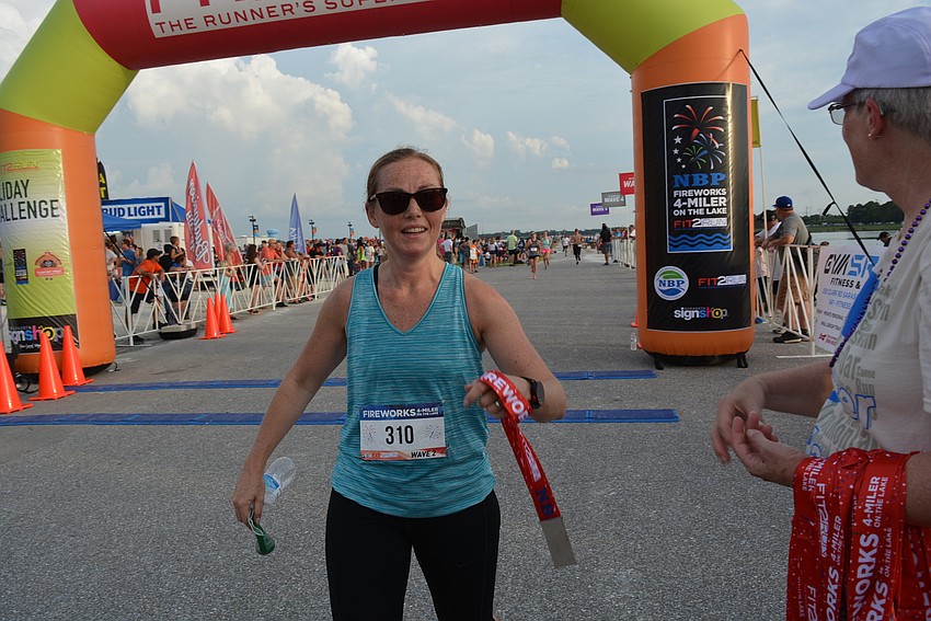 The Meadows' Joanna Rodger accepts a finisher's medal from volunteer Rhonda Gonzalez as she finishes the first ever Fireworks 4-Miler On The Lake.
