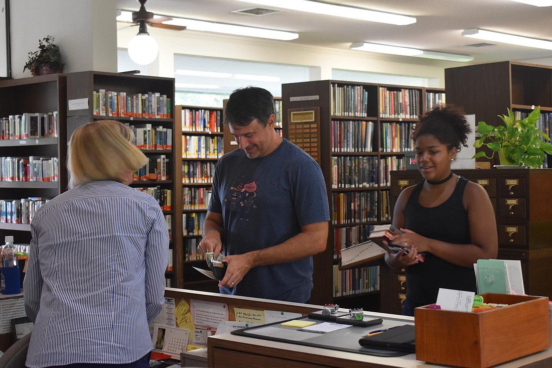 Volunteer librarian Linda Lutz helps Todd and Isabel Jordan check out books for their week.