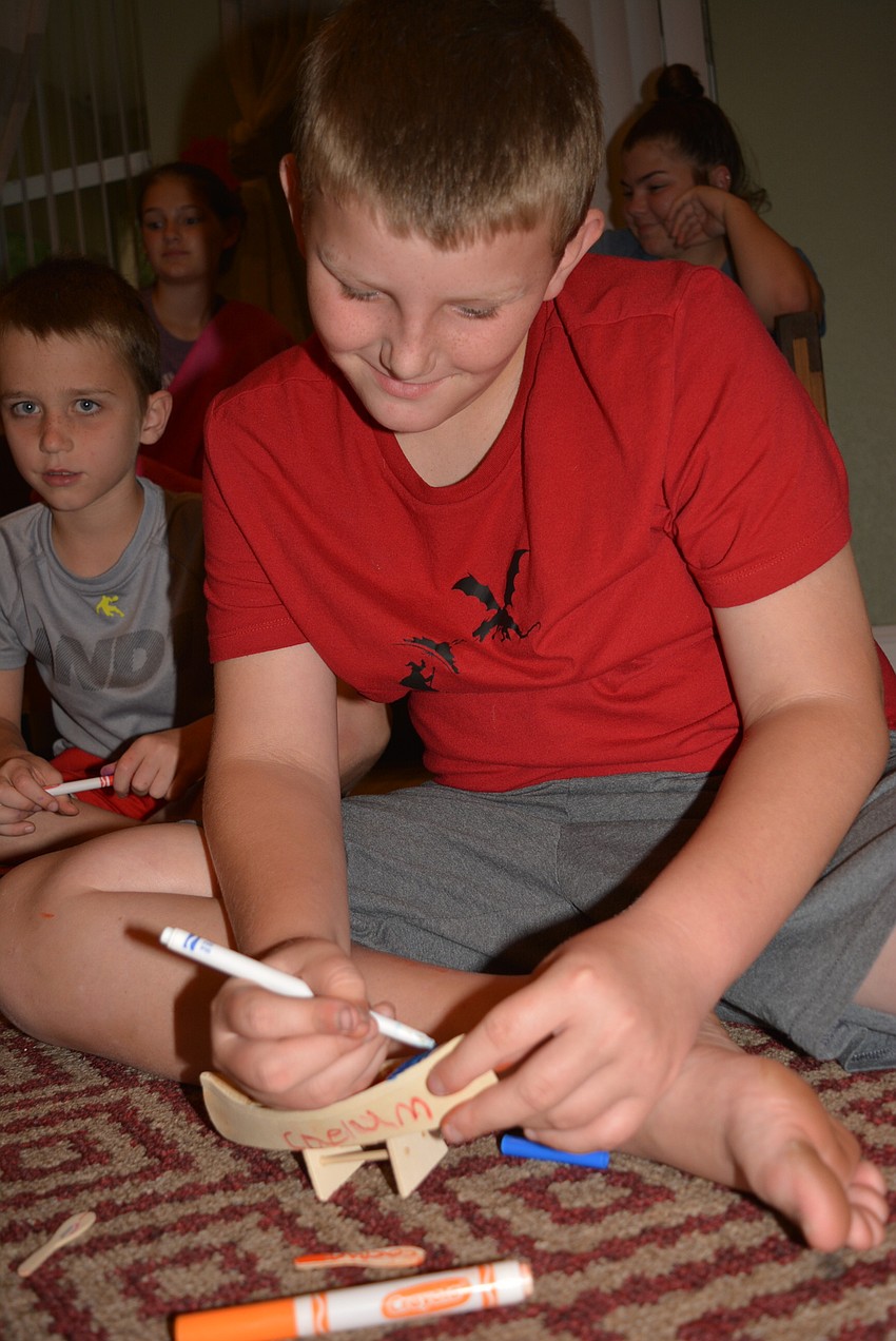 Dylan Lindauer, behind, watches as 10-year-old Caelum Brown finishes coloring his wooden boat.