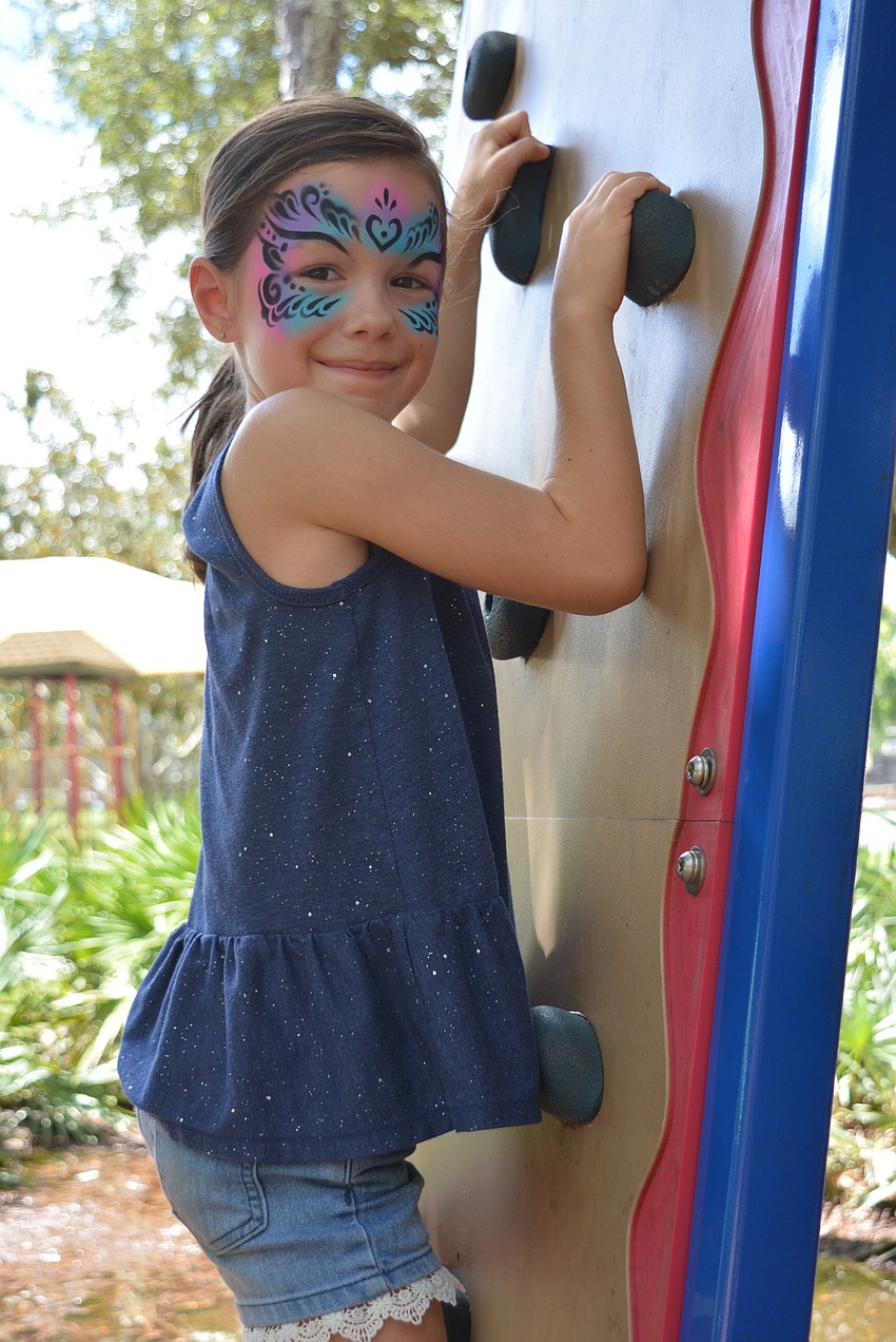 Seven-year-old Hannah Jennings, of Sarasota, tries the rock wall at the playground after face painting and lunch.