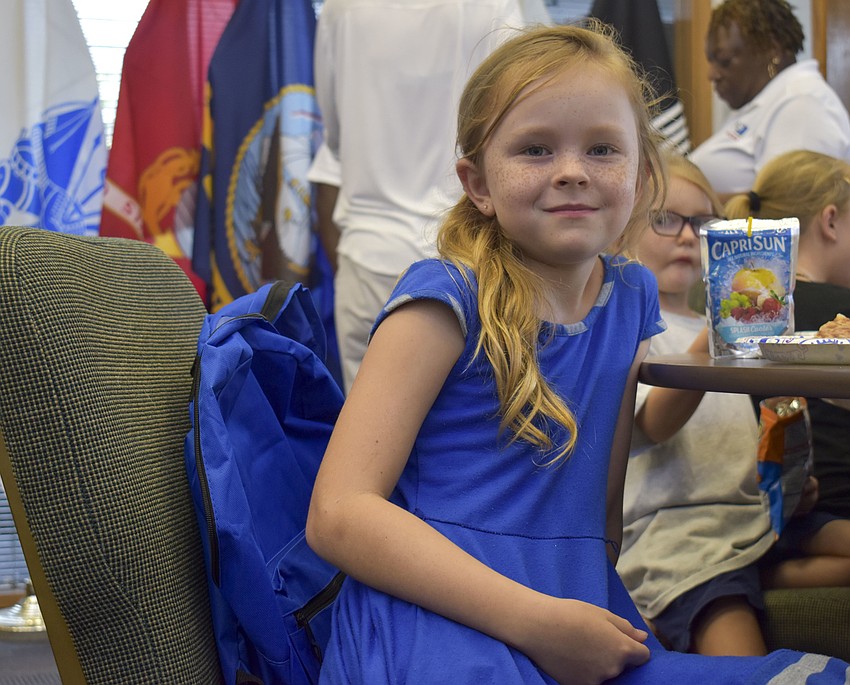 Erin Brett, 8, enjoys her dinner while she waits for her turn to grab a backpack.