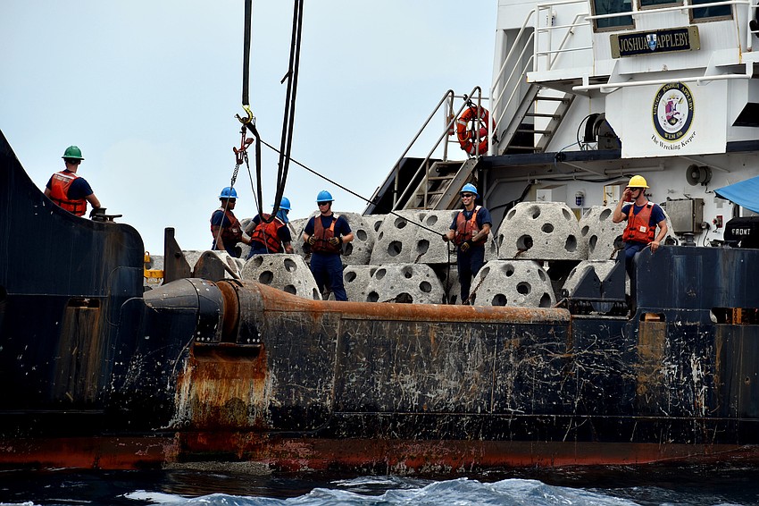 Crew members on the Joshua Appleby begin lowering reef balls into the ocean.