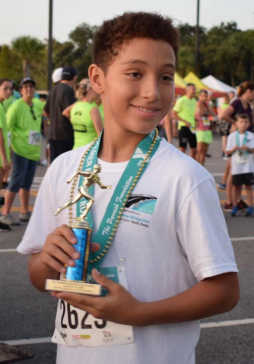 Esteban Benjoud, 11, shows off his trophy for being the first male to complete the kids race for 10 through 12 year olds during the Fort Hamer Bridge Run.