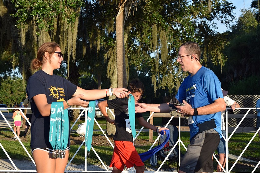 Manatee County Youth Rowing member Sarah Joseph, 15, left, hands a medal to a runner who completed his race during the Fort Hamer Bridge Run. This was Joseph's third year volunteering for the event.