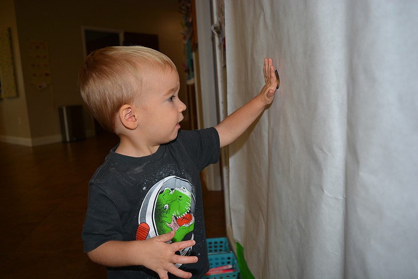 Two-year-old Aaron Free selects a praying mantis sticker for the mural wall, before going back for more stickers to add.