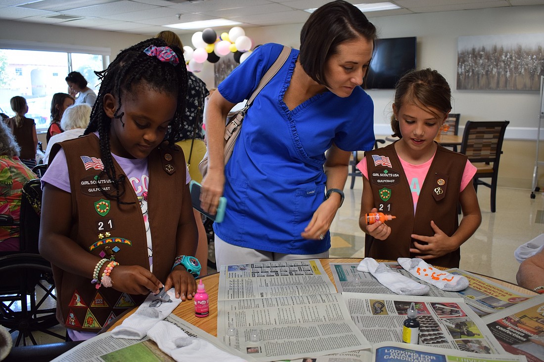 Girl Scouts Maia Bacchus, 8, left, and Olivia Hedrick, 7, right, use puffy paint to make non-slip socks for patients at Heartland Health Care Center as Hedrick&#39;s mom, Sara, watches as a parent volunteer.