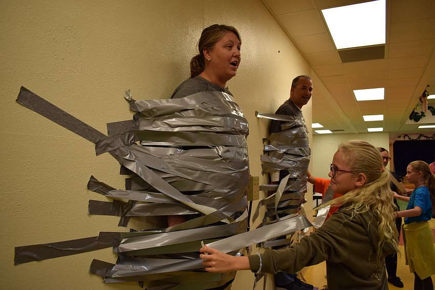 Braden River Elementary School fourth-grader Caitlin Motherway, 9, right, is one of the about 252 students who were able to tape Assistant Principal Krista Francies to a wall as a reward for completing their summer learning.