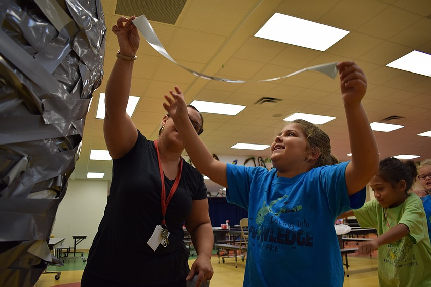 Braden River Elementary School paraprofessional Salvatrice Rizzo, left, helps second-grader Rosemary Aronin, 7, attach a piece of tape to Principal Joshua Bennett's shoulders.