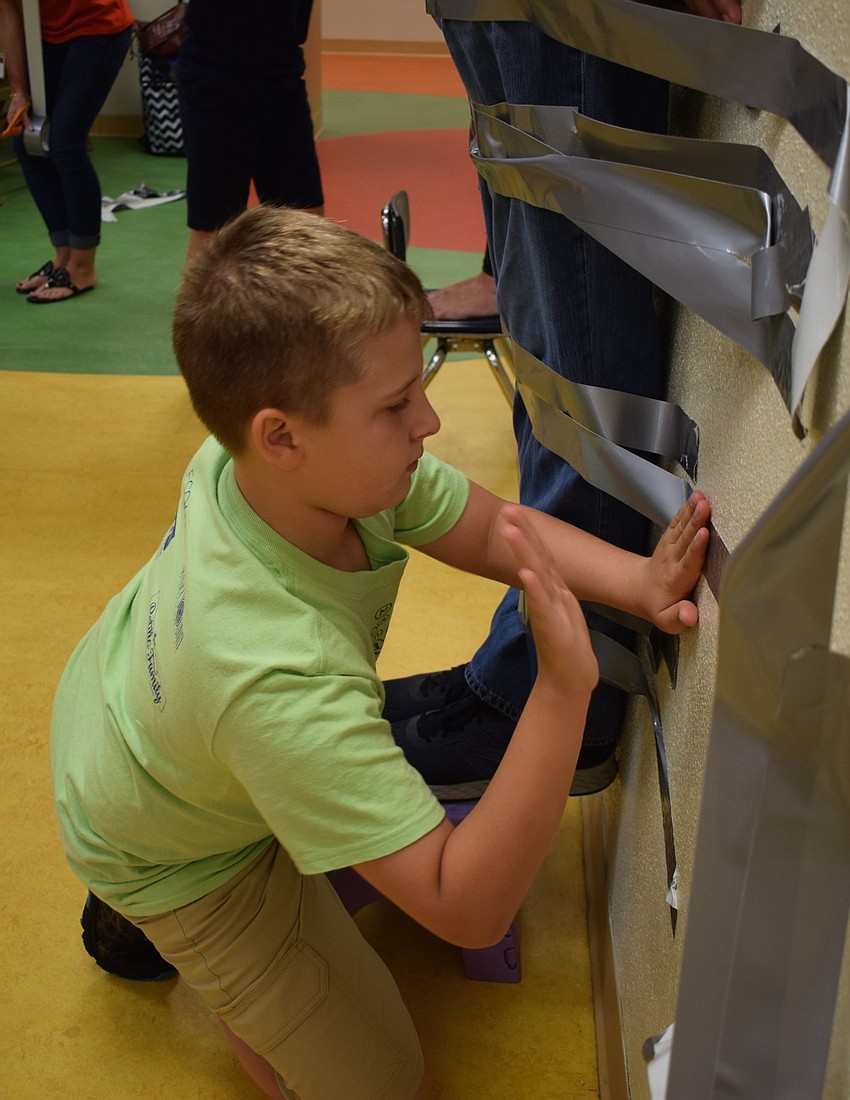 Braden River Elementary School fifth-grader Logan Santiago, 10, pounds tape to the wall to make sure it's secure.