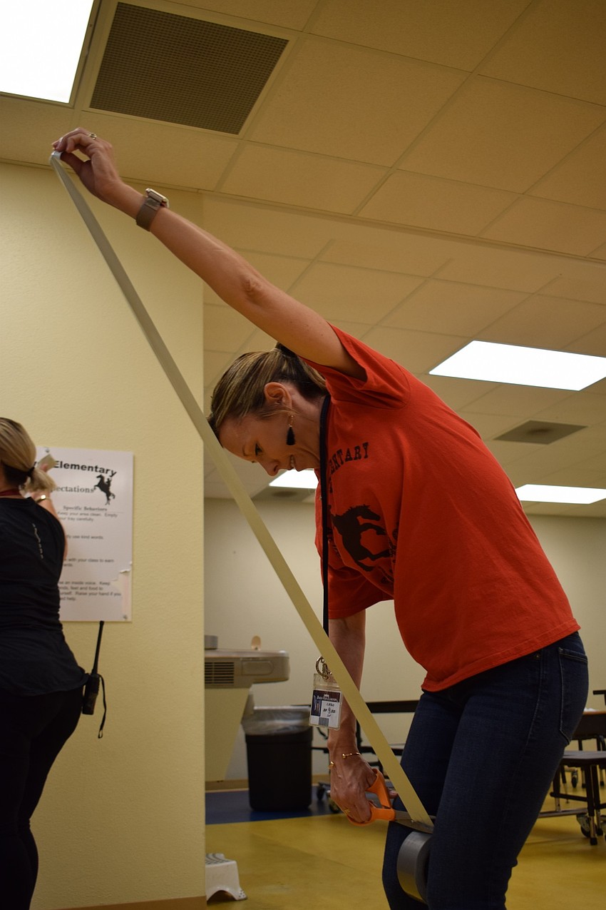 Braden River Elementary School office clerk Kelly Withers works to cut off a piece of tape to hand to students so they can tape it to Principal Joshua Bennett.