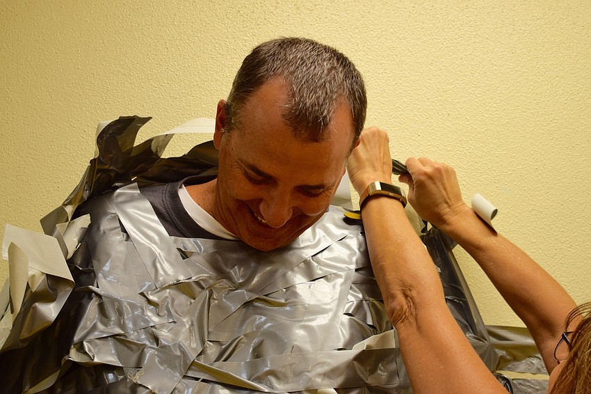 Braden River Elementary School Principal Joshua Bennett smiles as student support specialist Michele Jones works to peel him off the wall and free him from more than 252 pieces of duct tape students placed on him.