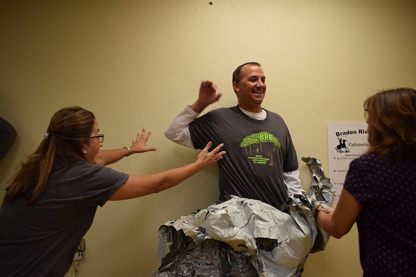 Braden River Elementary School kindergarten teacher Frances Vila, left, reaches out to Principal Joshua Bennett, center, as he starts to fall while student support specialist Michele Jones, right, peels the tape off Bennett.