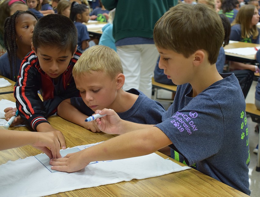 From left, Gilbert W. McNeal Elementary School fourth-graders Thiago Bravo, 9, Colt Smith, 10, and Hilel Yakich, 9, work together to outline a card on a piece of cloth to make eco-friendly food storage.