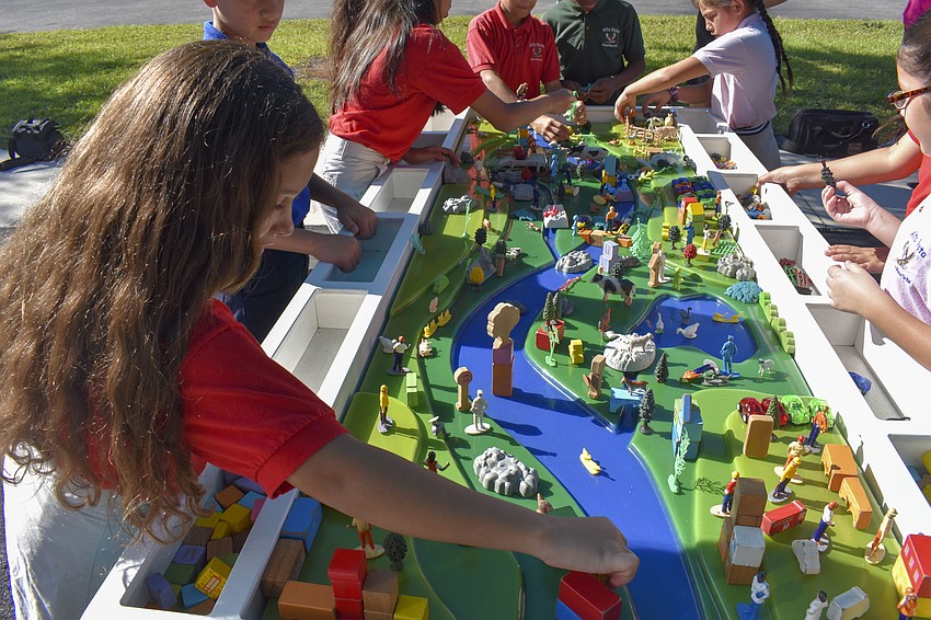 Rafaela Omega places a tree in the watershed diorama.