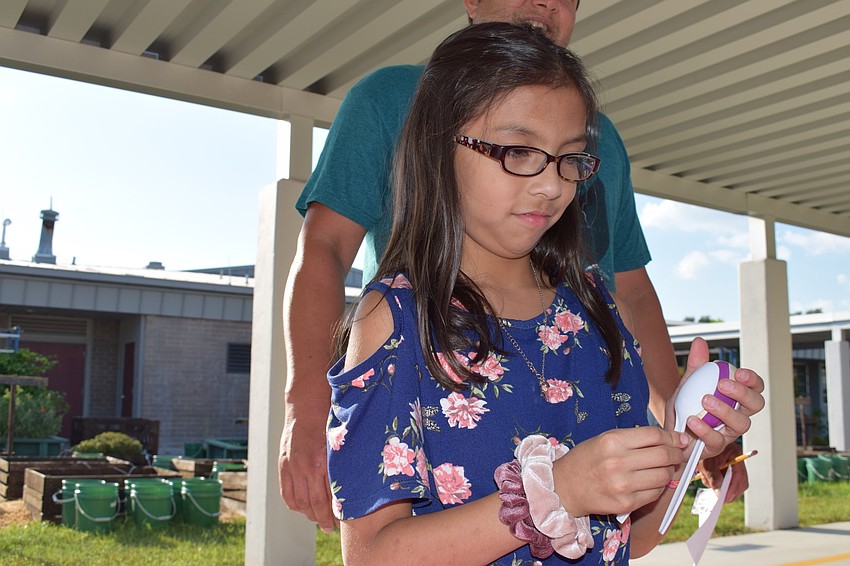 Third-grader Ana Marina makes a maraca out of plastic spoons and a purple plastic egg filled with rice.